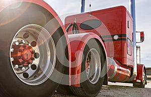 Classic red American semi truck in parking lot, detail of aluminum tandem axles with red hub caps. Low angle, rear view of big rig