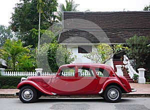 Classic red Citroen Traction Avant vintage car side view against backdrop of colonial heritage buildings