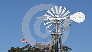 Classic retro windmill, bladed rotor and USA flag against blue sky. Vintage water pump wind turbine, power generator on