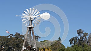 Classic retro windmill, bladed rotor and USA flag against blue sky. Vintage water pump wind turbine, power generator on