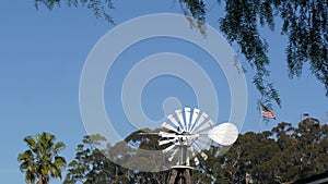 Classic retro windmill, bladed rotor and USA flag against blue sky. Vintage water pump wind turbine, power generator on livestock