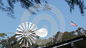 Classic retro windmill, bladed rotor and USA flag against blue sky. Vintage water pump wind turbine, power generator on livestock