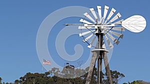 Classic retro windmill, bladed rotor and USA flag against blue sky. Vintage water pump wind turbine, power generator on livestock