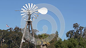 Classic retro windmill, bladed rotor and USA flag against blue sky. Vintage water pump wind turbine, power generator on livestock