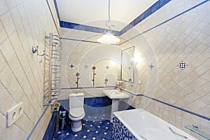 Classic rich beige bathroom with bathtub, toilet and sink with mirror. The walls are white tile with a pattern