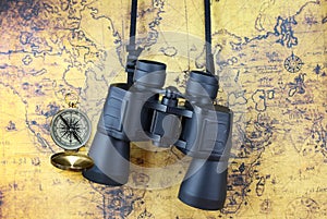 Classic round compass and binoculars on background of old vintage map of world