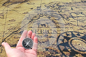 Classic round compass in hand on background of old vintage map