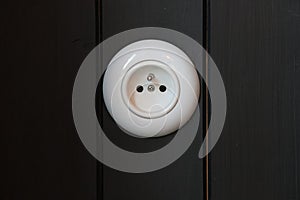 A classic round white electrical socket is mounted on vertical black wooden paneling