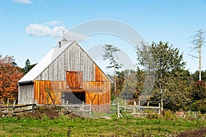 A classic scene of a worn barn in a pasture with blue sky and sun