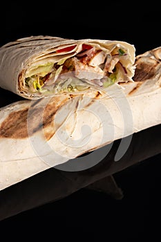 Classic shawarma kebab pita with chicken and vegetables and sauce on a black background. in section