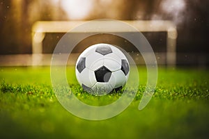 Classic soccer ball in sunset  with typical black and white pattern, placed on stadium turf. Traditional football ball on the