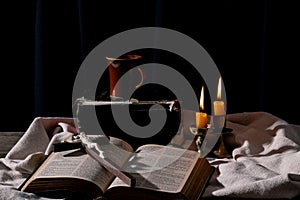 Classic Still Life with an Old Book, Holy Bible, Crucifix, and Lit Candle on a Wooden Table