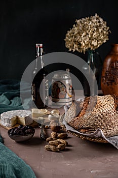 Classic still life with rustic bread, hydrangea, beer, cheese, black olives, green napkins on a brown table and dark background.
