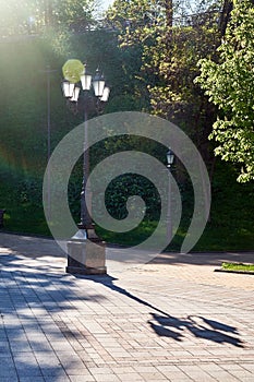 A classic street lamp casts a shadow on a park path on a sunny day