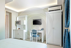 Classic style white and blue interior of hotel room with kitchen module cupboard cabinet, wardrobe and TV table in single space