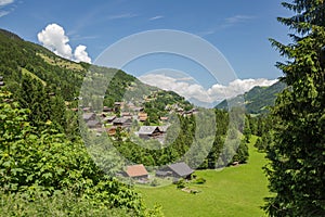 Classic swiss chalet in the middle of green alpine meadows . Cozy rural village Champery in Switzerland. Bright blue sky and white