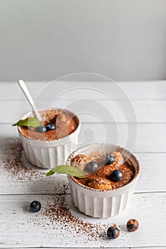 Classic tiramisu dessert with blueberries, mint in white jar on grey background. Flat lay concept. Vertical