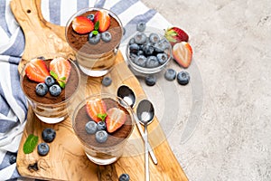 Classic tiramisu dessert with blueberries and strawberries in a glass on concrete background