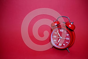 Classic vintage mechanical retro red alarm clock on red background at almost 7 o`clock with copy space. Isolated object.