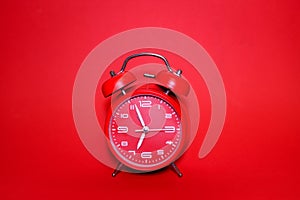 Classic vintage mechanical retro red alarm clock on red background at almost 7 o`clock with copy space. Isolated object.