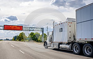 Classic white big rig semi truck with large cab sleeping compartment transporting cargo in dry van semi trailer running on the