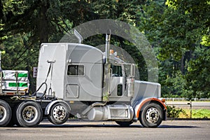 Classic white big rig semi truck tractor with loaded flat bed semi trailer standing on the rest area parking lot parallel to the