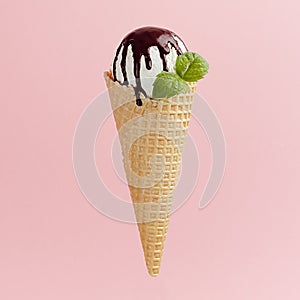 Classic white ice cream in crisp waffle cone with chocolate sauce, mint leaf on pink background, square, closeup.
