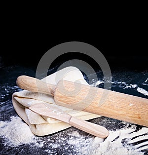 Classic wooden rolling pin with freshly prepared dough and dusting of flour on black background