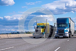 Classic yellow and blue modern semi trucks side by side on the r