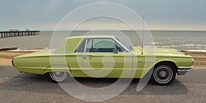 Classic Yellow Thunderbird motor car parked on seafront promenade.