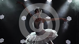 Classical ballet choreography perfoming by young beautiful graceful ballerina in white tutu. Shot in a darkness on