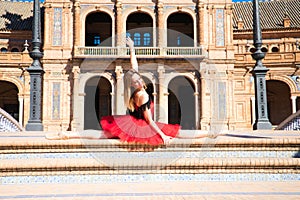 Classical ballet dancer in red tutu with her legs open on the steps of a park and her arms outstretched. Classical ballet