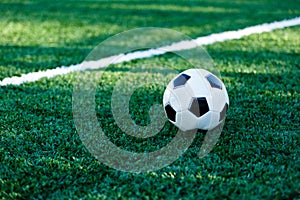 Classical black and white football ball on the green grass of the field. Soccer game, training, hobby concept