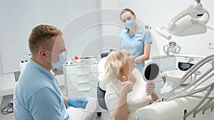 classical dental coloring for determining color of teeth dental clinic doctor hands over mirrors middle aged woman