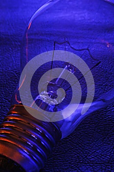 Classical electric tungsten light bulb on a textured blue background with red highlights on the lamp body.