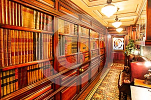 Classical library room with leather armchair, wooden table and bookcase. English classic style