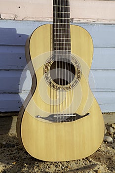 Classical parlour guitar resting against blue and pink beach hut