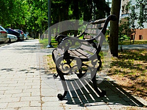 Classical shape old wooden and cast iron park bench along concrete sidewalk