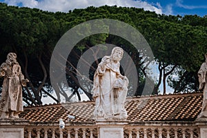 Classical statues on Vatican building terrace amidst surveillance technology, Rome.