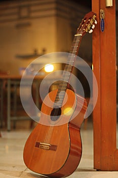 a classical wooden guitar propped against a wooden wall