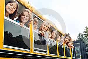 Classmates going to school by bus leaning out of the window smiling happy