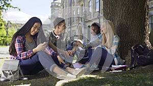 Classmates sitting under tree, girl touching guys arm, friendship and flirt