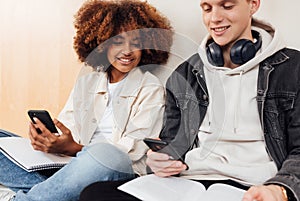 Classmates with smartphones preparing their assignments while sitting at wall