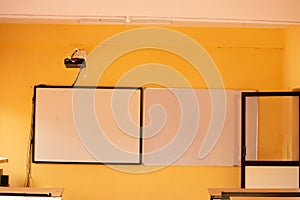 Classroom with yellow walls and white boards with projector.