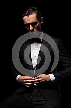Classy businessman in black suit posing seated in dark studio