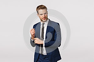 Classy good-looking blond bearded young male entrepreneur in suit, adjusting sleeves of jacket and looking away with