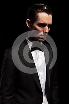 Classy man in tuxedo looking away in dark studio