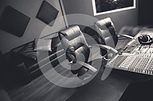 Classy professional recording studio setup, large desk with mixing console and two chairs, window for vocal booth, sofa