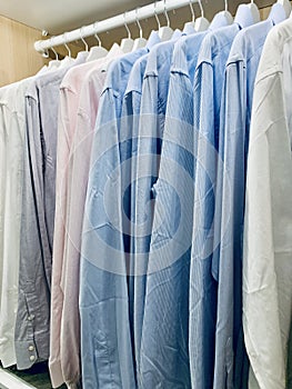 Classy, stylish, colorful men's formal long sleeve shirts neatly arranged and organized in a row on a clothes rack