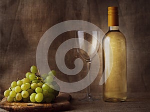 Claster of fresh juicy white grapes on a wooden board and glass and bottle of white wine on hessian cloth background. Still life,